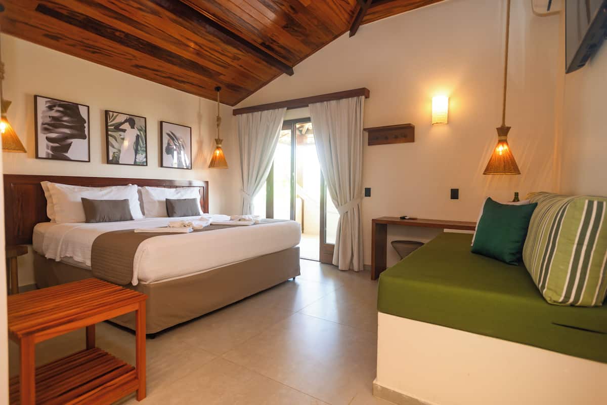 Une chambre à coucher avec un lit, un canapé, une table en bois et une fenêtre avec des rideaux.