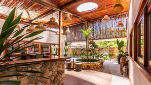 A spacious lobby with a stone reception desk, hanging wicker lamps, and a bamboo fence. - Pousada Vila Vagalume (Trairi)