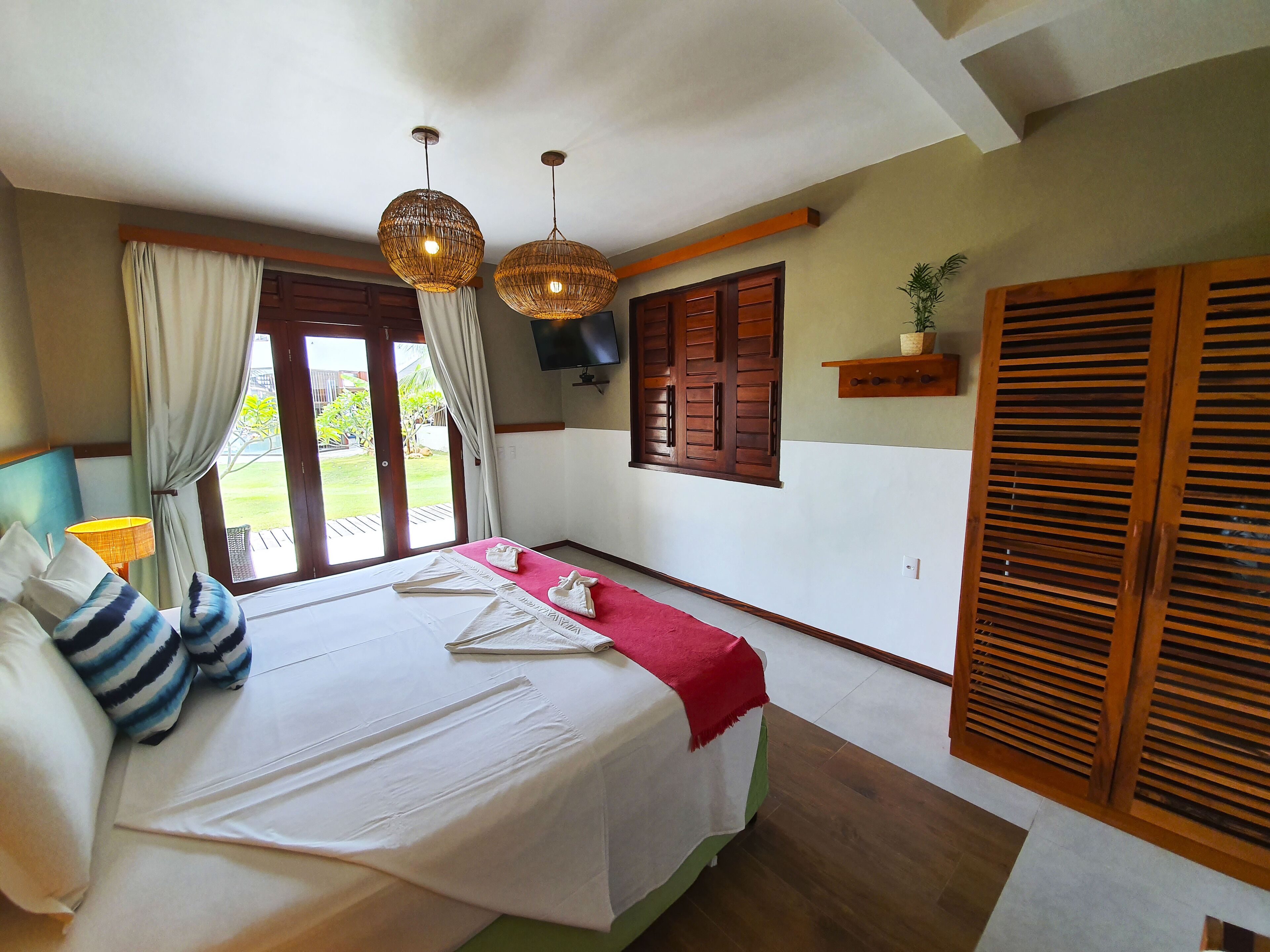 Habitación de hotel con cama, cortinas, televisor, contraventanas de madera y vista al exterior.
