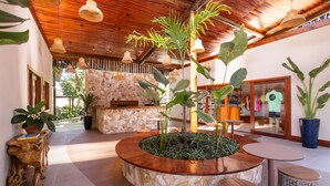 A circular wooden table surrounded by potted plants, with a stone wall and wooden ceiling in the background. - Pousada Vila Vagalume (Trairi)