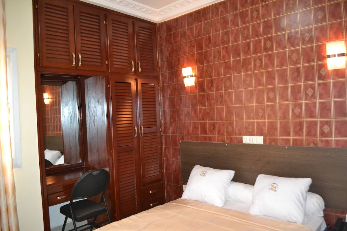 A bedroom with a wooden wardrobe, a desk, and a bed with two pillows.
