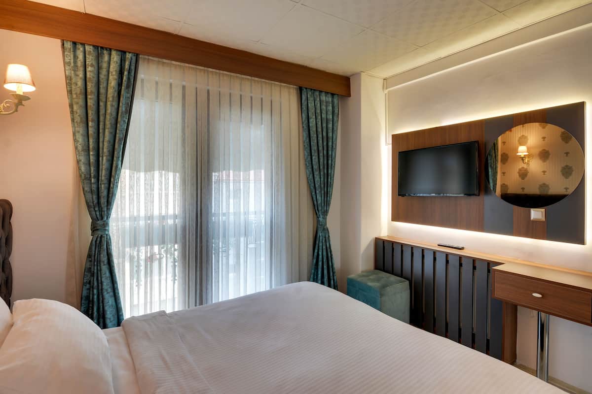 Ein Hotelzimmer mit einem großen Bett, einem flachbildfernseher an der Wand, einem Holztisch und einem kleinen Hocker.