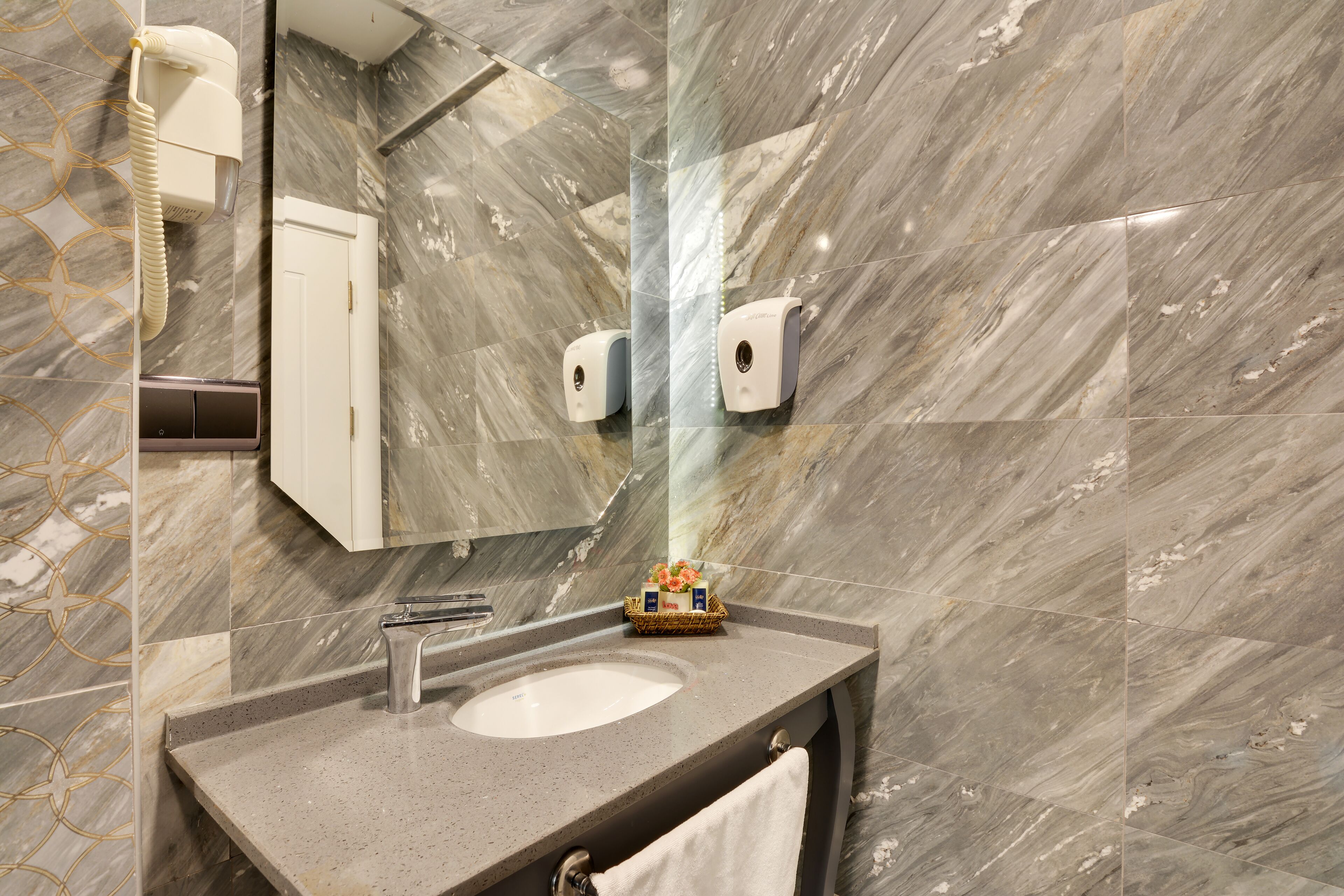 A bathroom with a marble floor, a sink, a mirror, a towel rack, and a hand dryer.