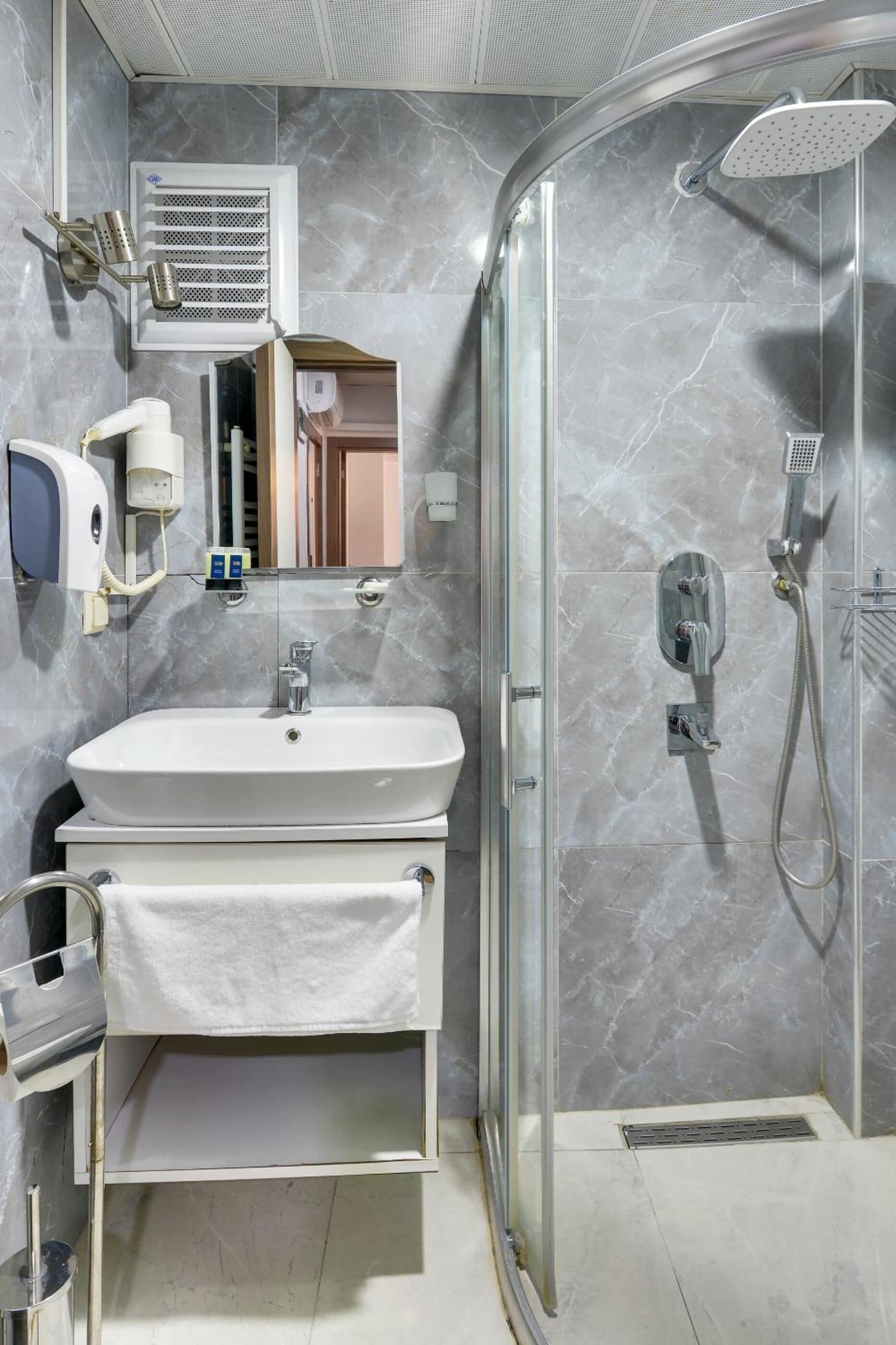 A modern bathroom with a glass-enclosed shower, a white sink, and a towel rack.