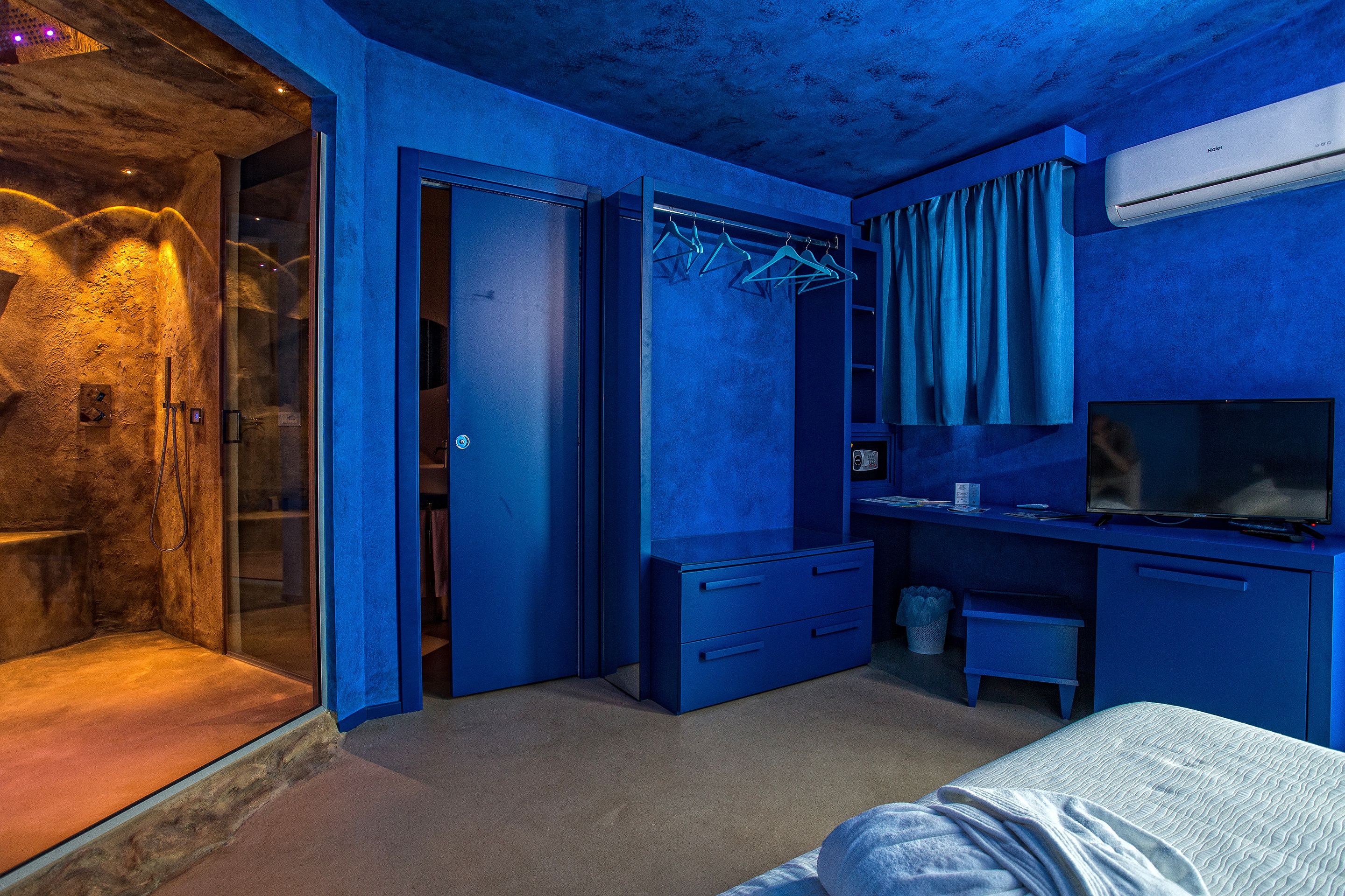 Une pièce avec un mur en pierre, une armoire bleue, un lit et un téléviseur.