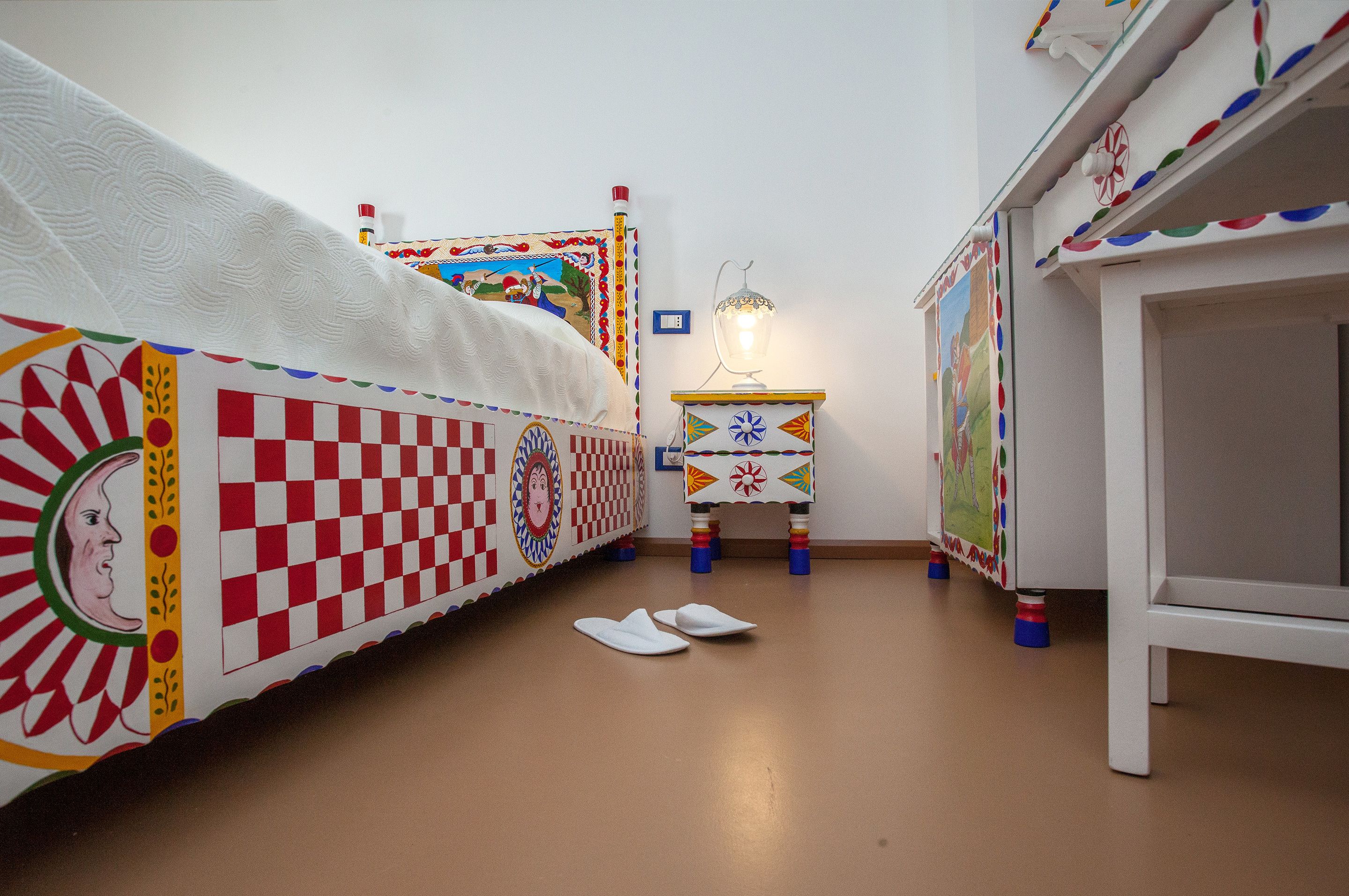 A child's bedroom with a checkered bedspread, a small bedside table with a lamp, and a colorful wall decoration.