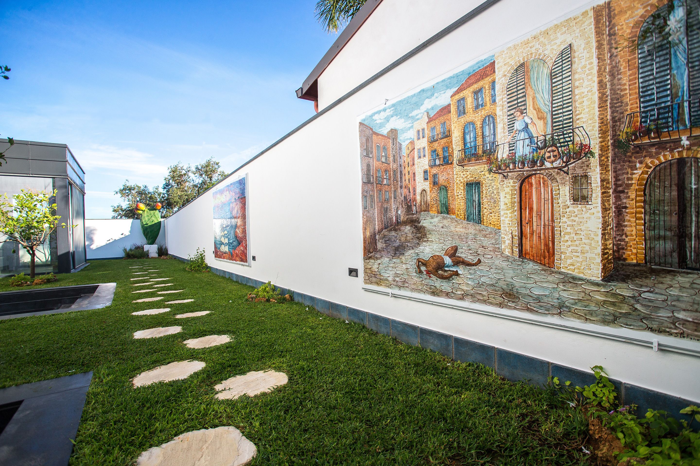 A modern building with a mural of a street scene, a pathway with stepping stones, and a small garden area.