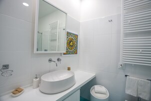 Un baño moderno con un lavamanos grande y blanco, un espejo y una zona de ducha.
