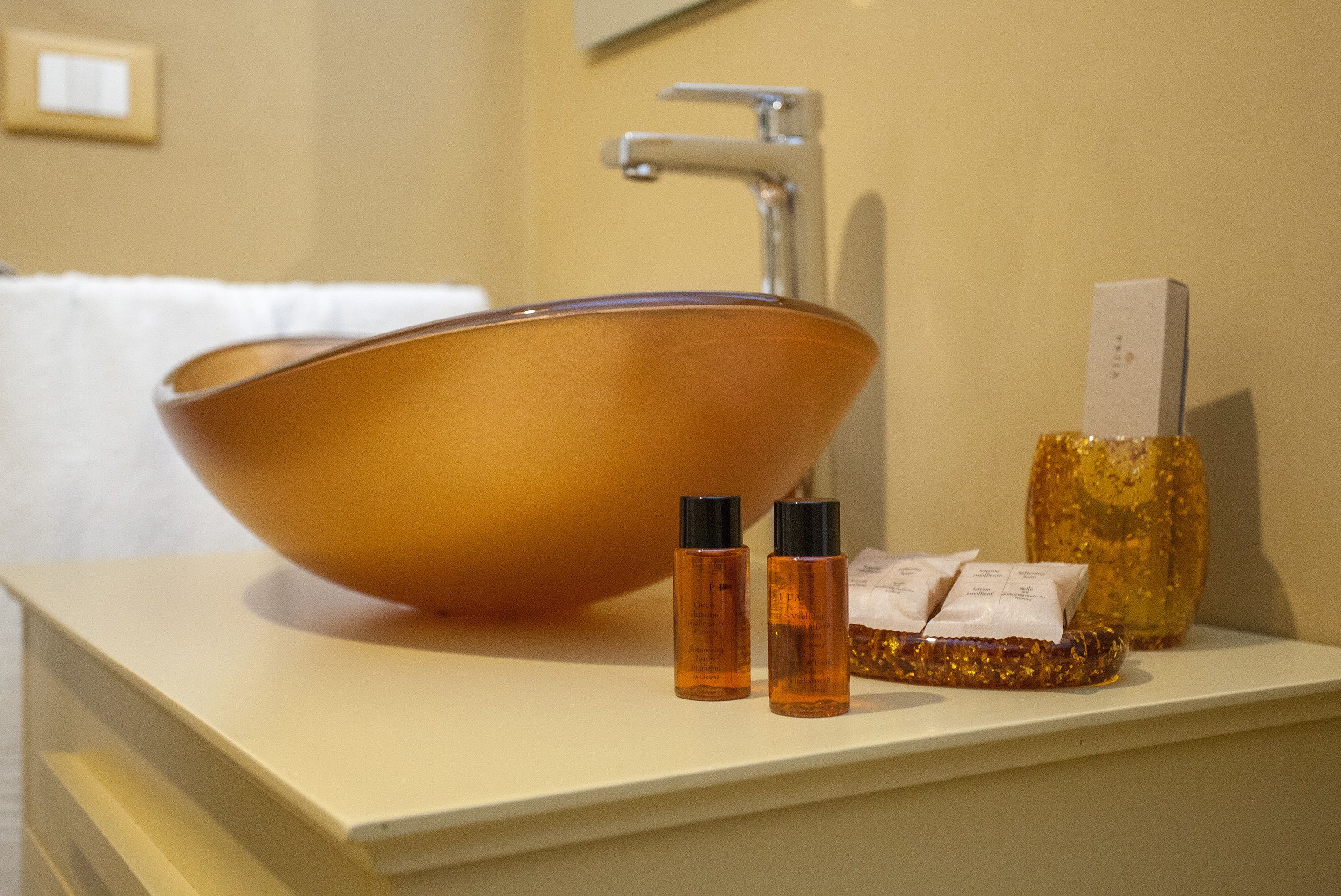 A bathroom with a large copper sink, two small bottles, and a decorative item on the counter.