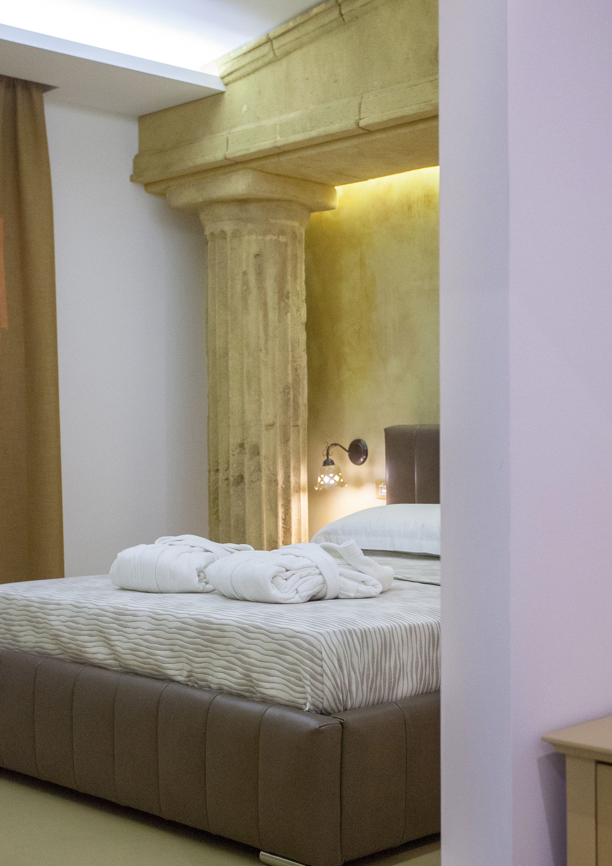 A bedroom with a large bed, a headboard, a nightstand, and a wall-mounted lamp.