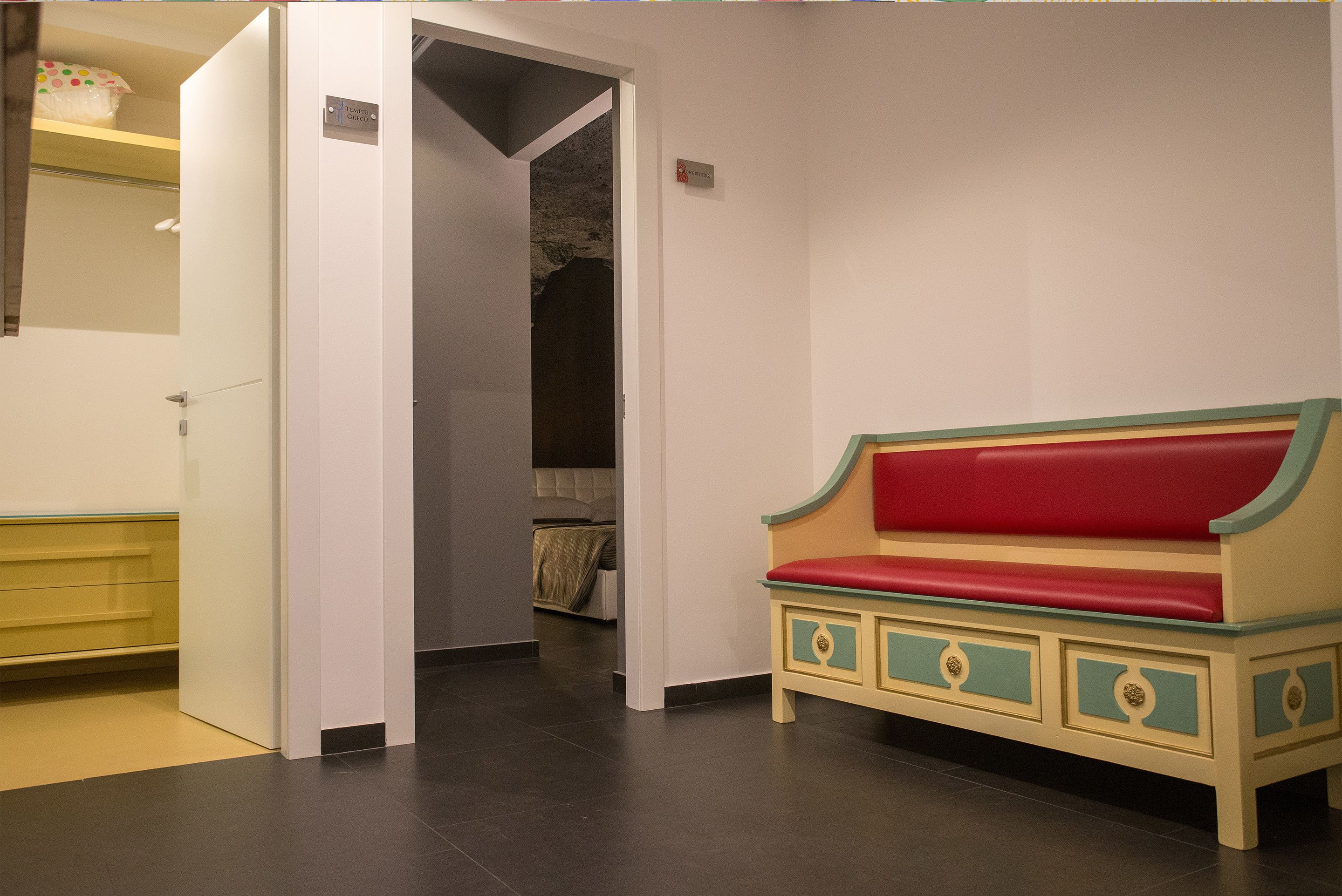 A room with a red and green bench, a white door, and a visible closet with a bed.