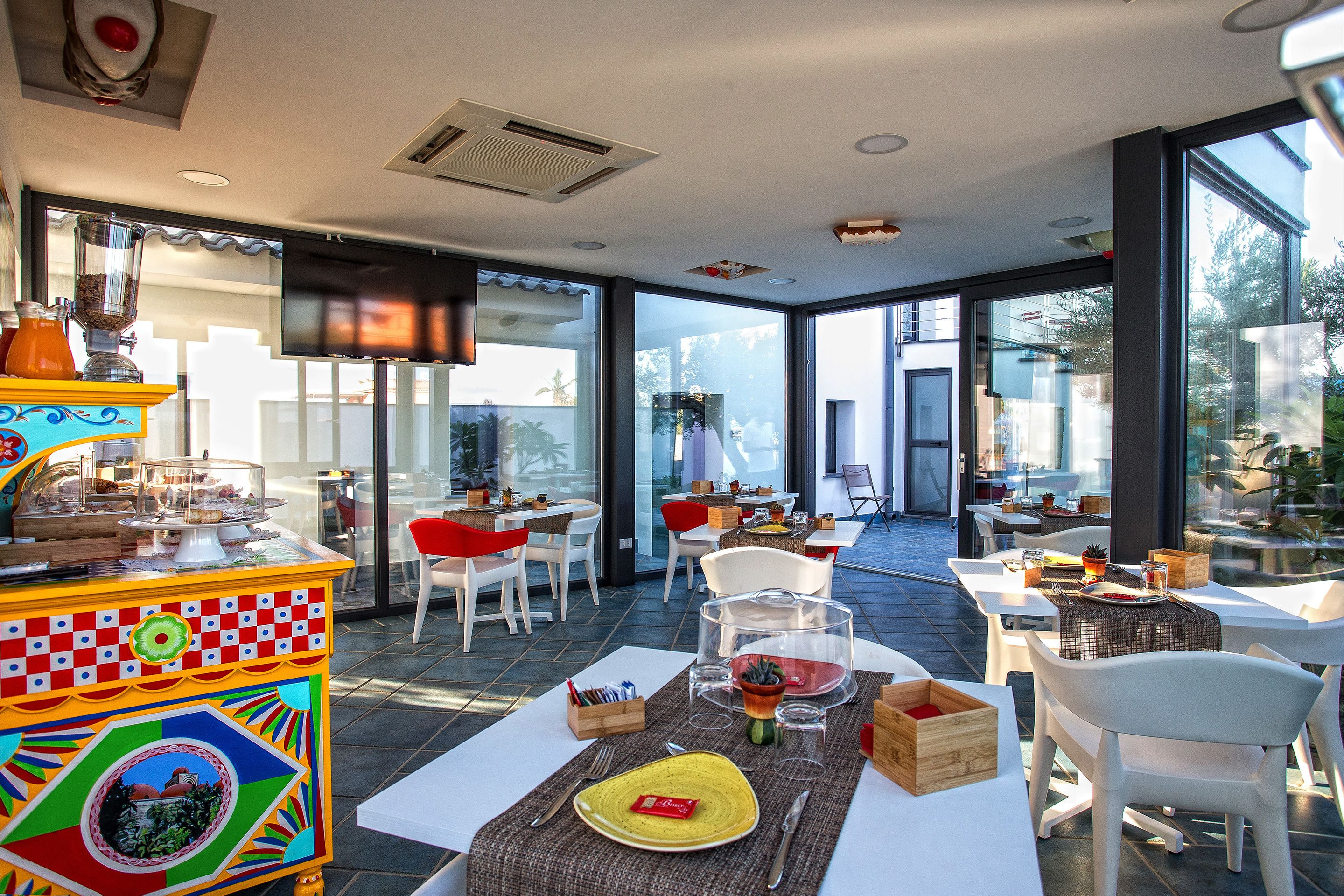Un comedor moderno con un carrito llamativo, sillas blancas y un amplio ventanal con vistas al exterior.