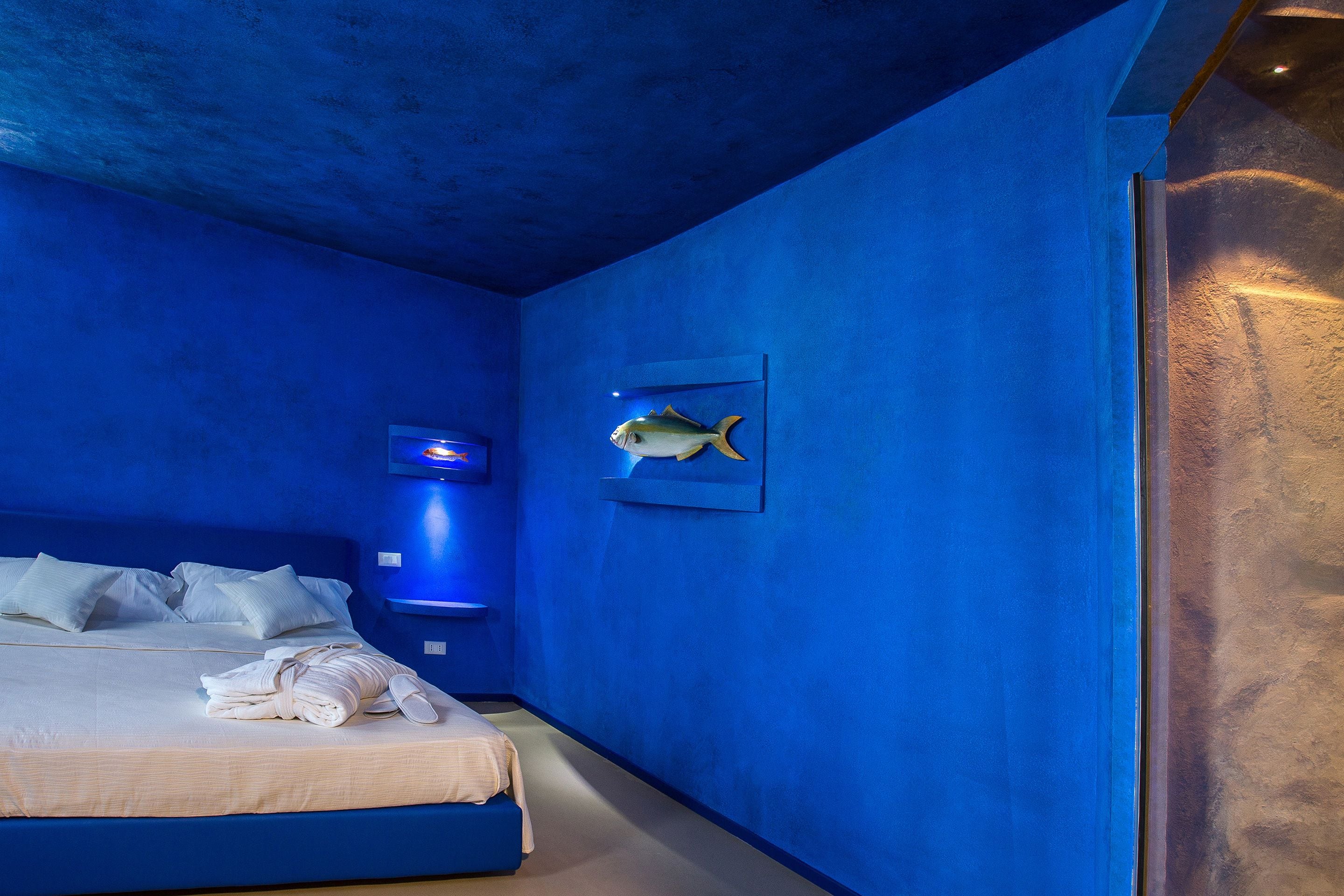 A room with a bed, a wall-mounted fish decoration, and a blue wall.