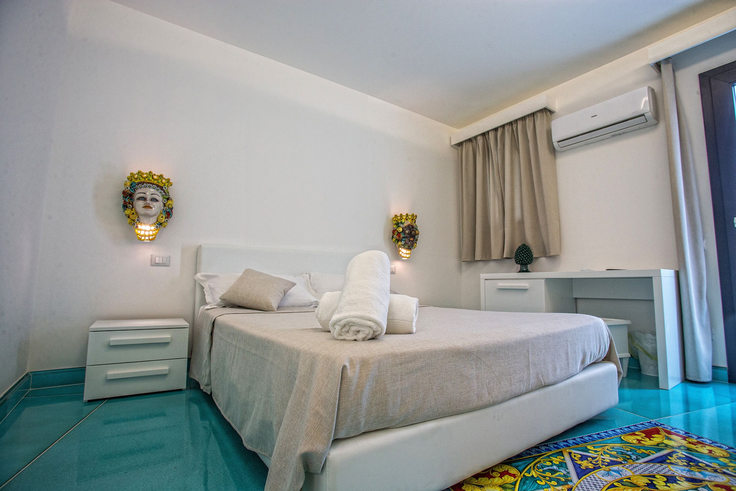 A bedroom with a bed, nightstands, a desk, and an air conditioning unit.