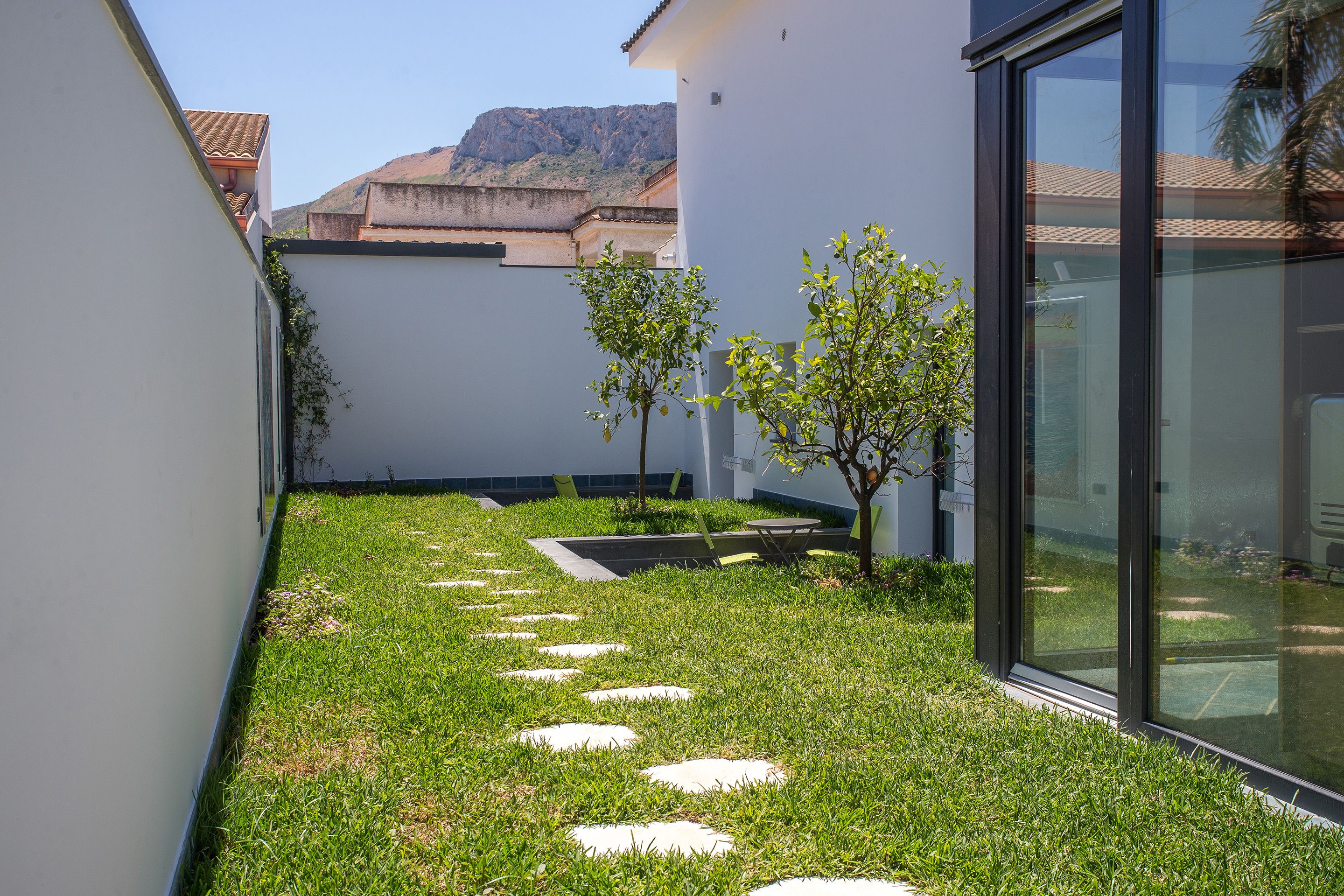 A modern building with a glass facade, a small garden area with stepping stones, and a view of a mountain in the background.