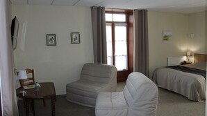 A hotel room with a bed, a chair, a table with a lamp, and a window with curtains. - Auberge la Source (Cieux)