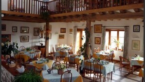 A spacious dining area with multiple tables and chairs, wooden beams on the ceiling, and various framed pictures on the walls. - Auberge la Source (Cieux)