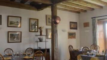 A dining area with wooden tables and chairs, a high ceiling with exposed beams, and framed artwork on the walls.
