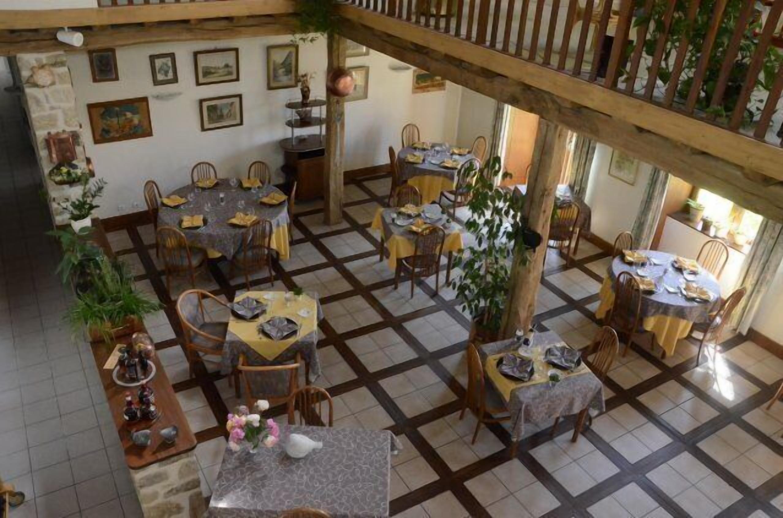 Un espace repas comprenant plusieurs tables et chaises, des poutres en bois et des œuvres d’art encadrées accrochées aux murs.