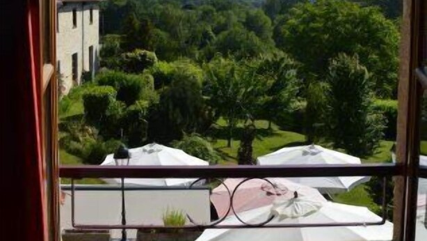 A balcony with a view of a green landscape, including trees and a building in the distance. - Auberge la Source (Cieux)