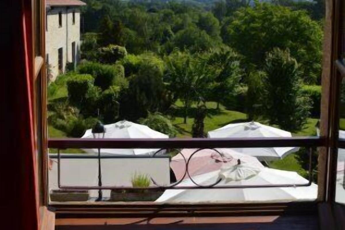 Un balcón con vista a un paisaje verde, que incluye árboles y un edificio a lo lejos.