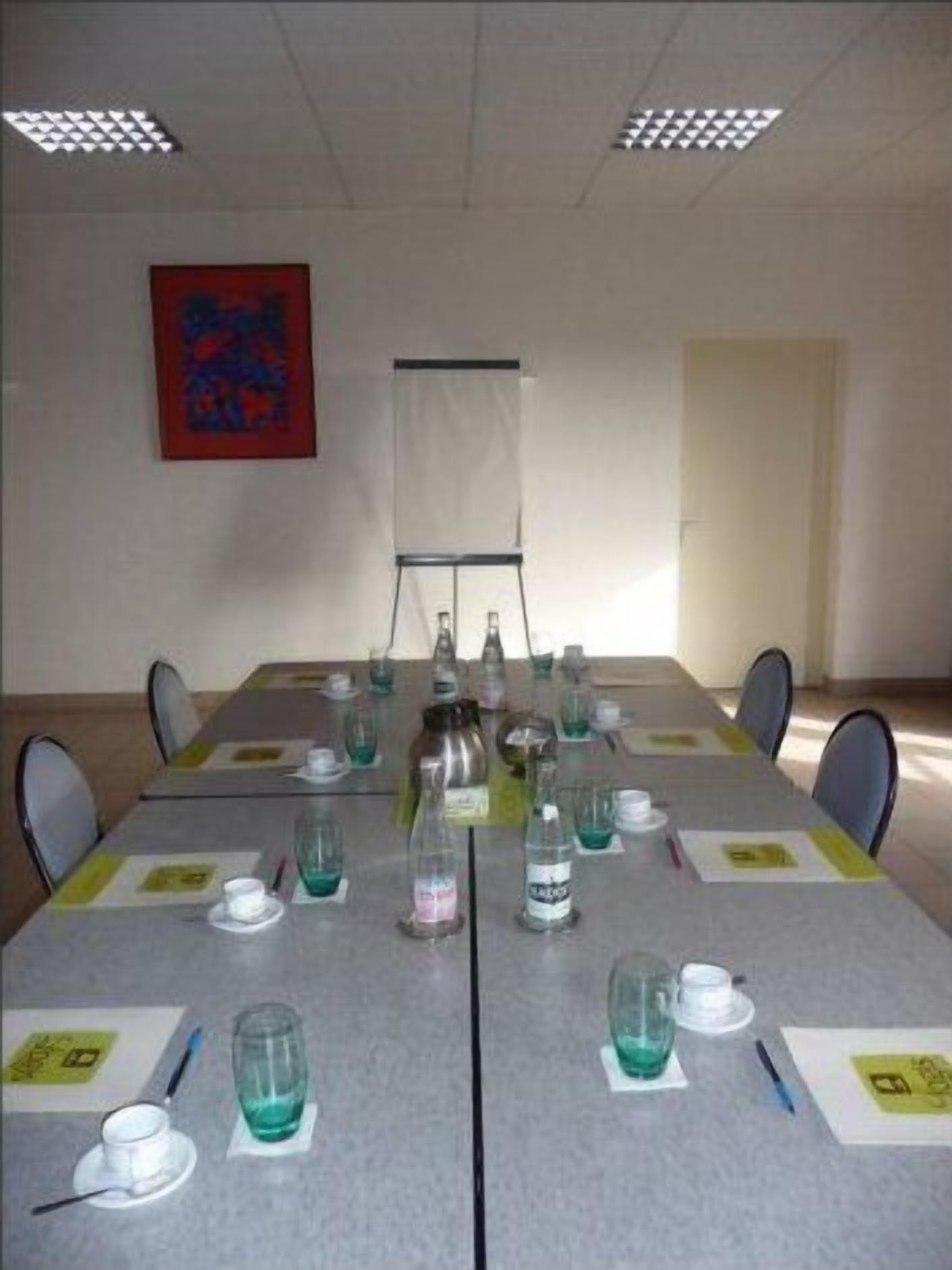 Une salle de conférence avec une longue table, des chaises, un écran de projection et un tableau accroché au mur.
