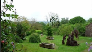 A garden with various plants and a stone structure. - Auberge la Source (Cieux)