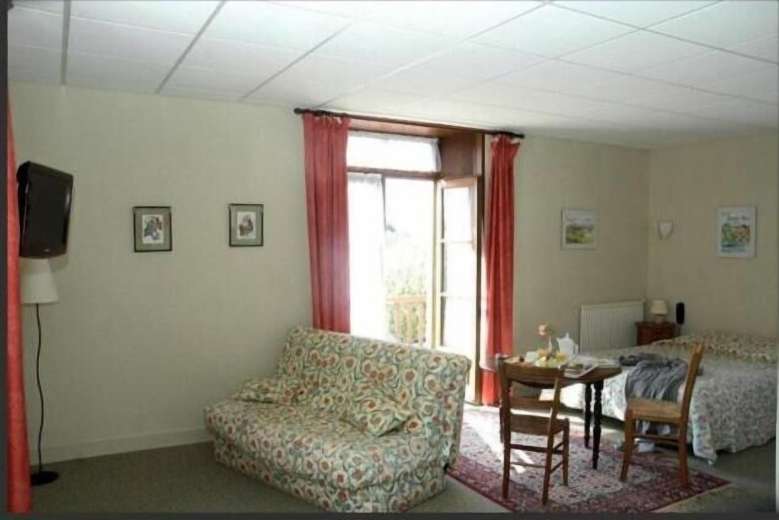 A room with a sofa, a small table with chairs, a bed, and a television on the wall.