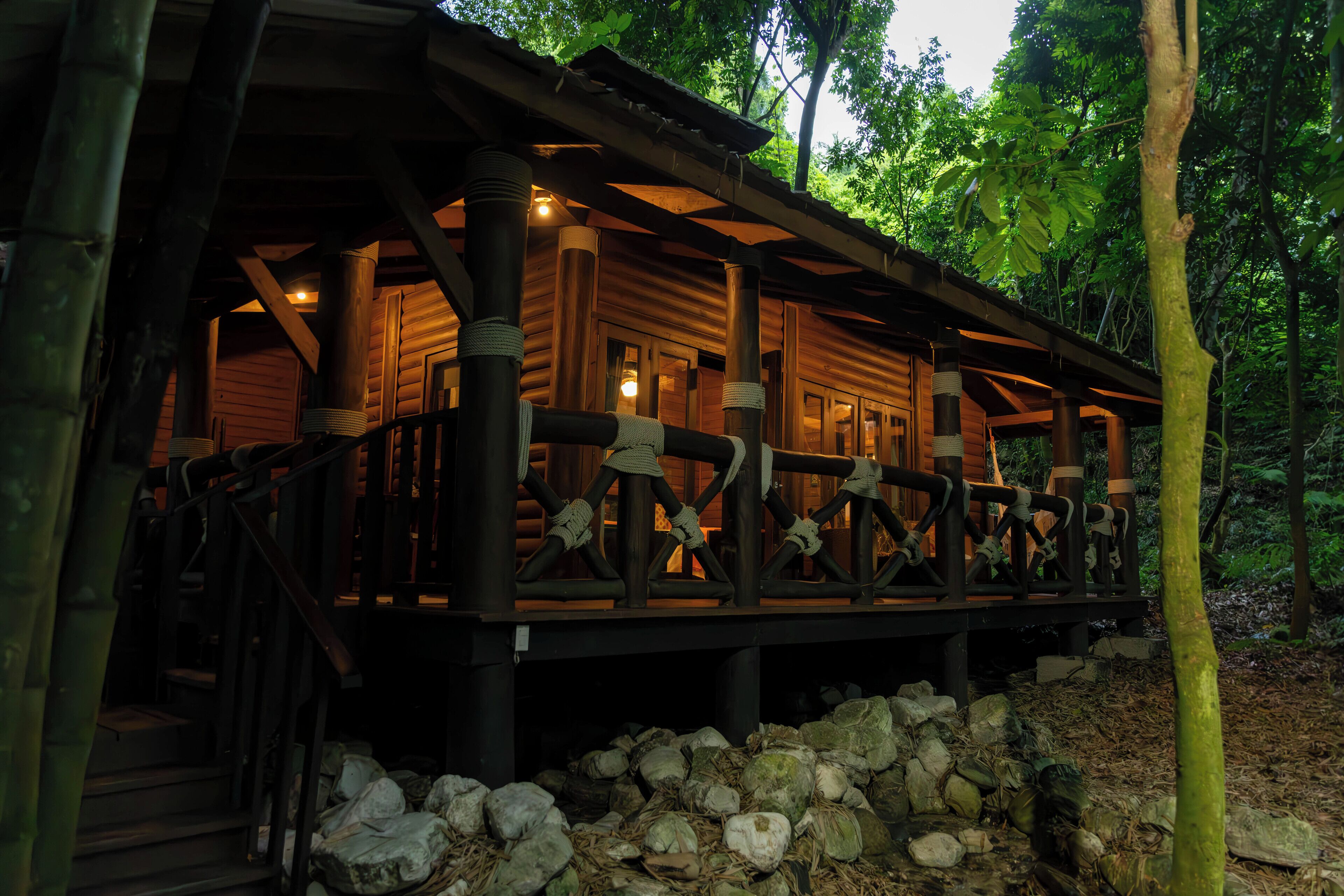A wooden cabin with a porch and stairs, surrounded by trees.