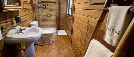 Une salle de bain rustique, aménagée dans une cabane en bois, avec un lavabo, des toilettes et une douche.