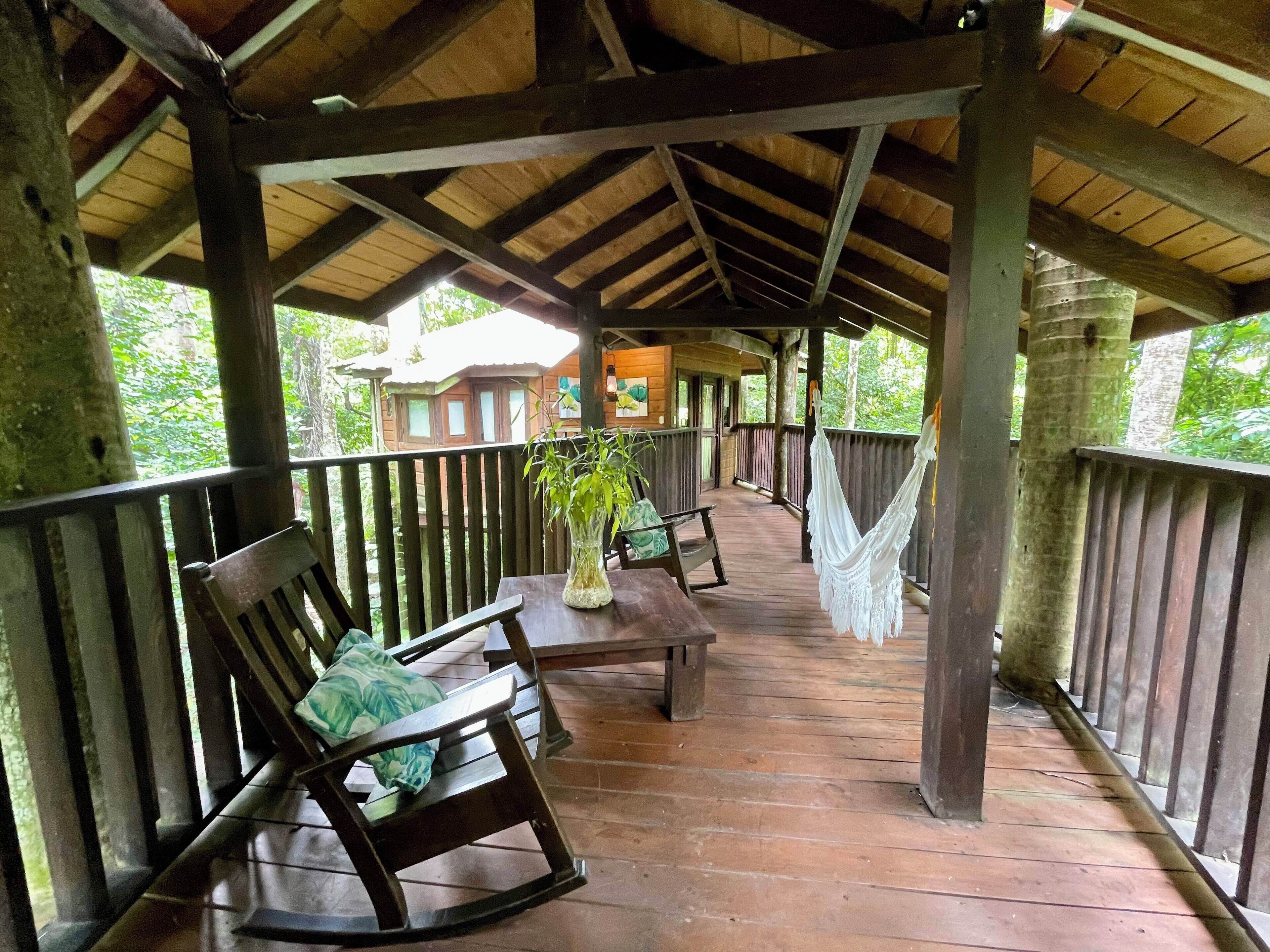 A covered wooden deck with benches and a hammock, overlooking a lush green landscape.