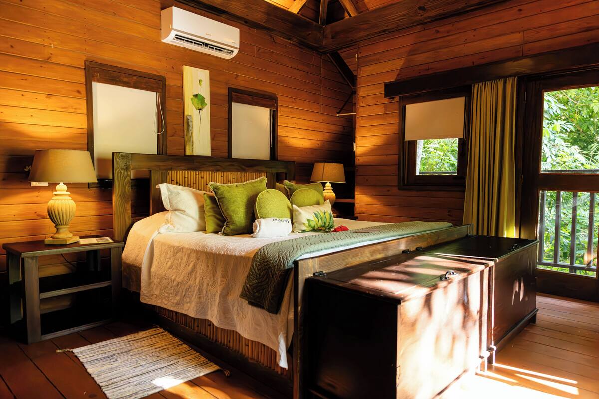 Un dormitorio de cabaña de madera con una cama, lámparas de noche, un aparador y una ventana con cortinas.