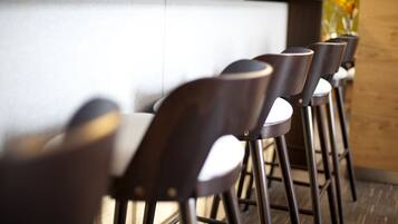 A row of wooden bar stools with metal legs, arranged in a line against a wall with a wooden panel and a white surface.