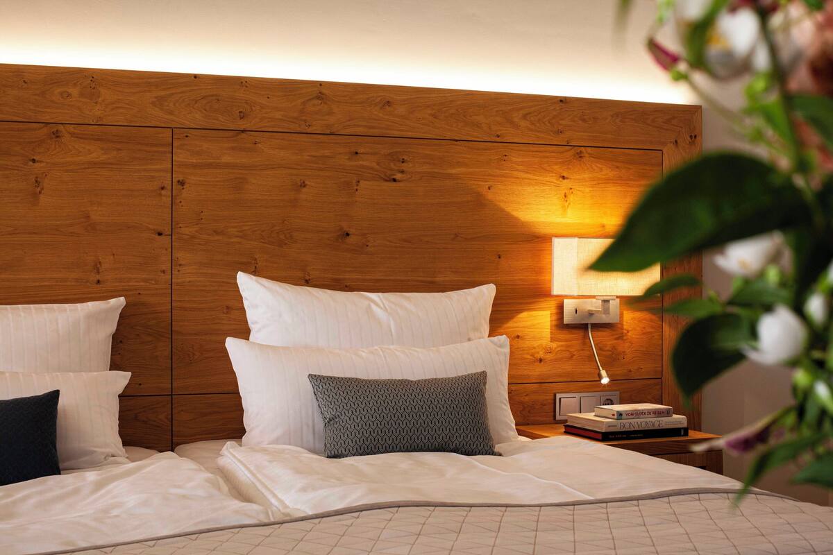 A neatly made bed with white and gray pillows, a wooden headboard, and a bedside table with a lamp and books.