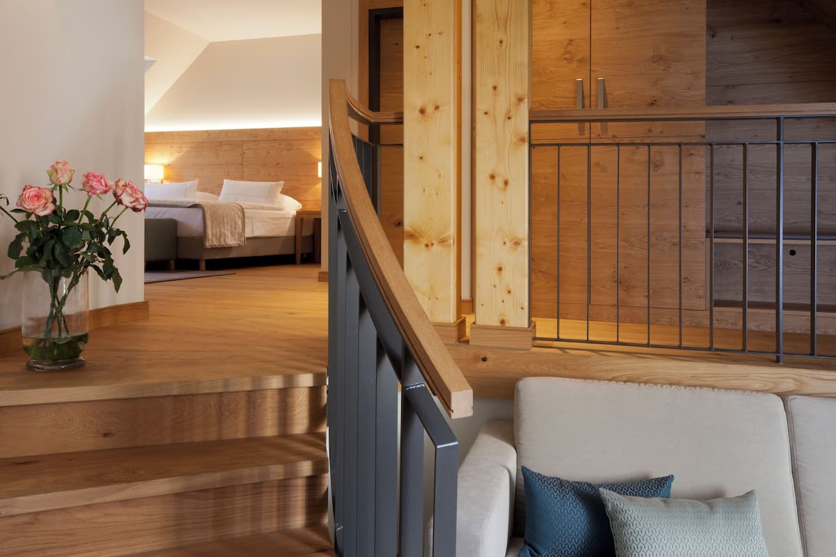 A modern interior with a wooden staircase, a cozy seating area, and a bedroom with a bed and bedside table.