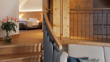 A modern interior with a wooden staircase, a cozy seating area, and a bedroom with a bed and bedside table.