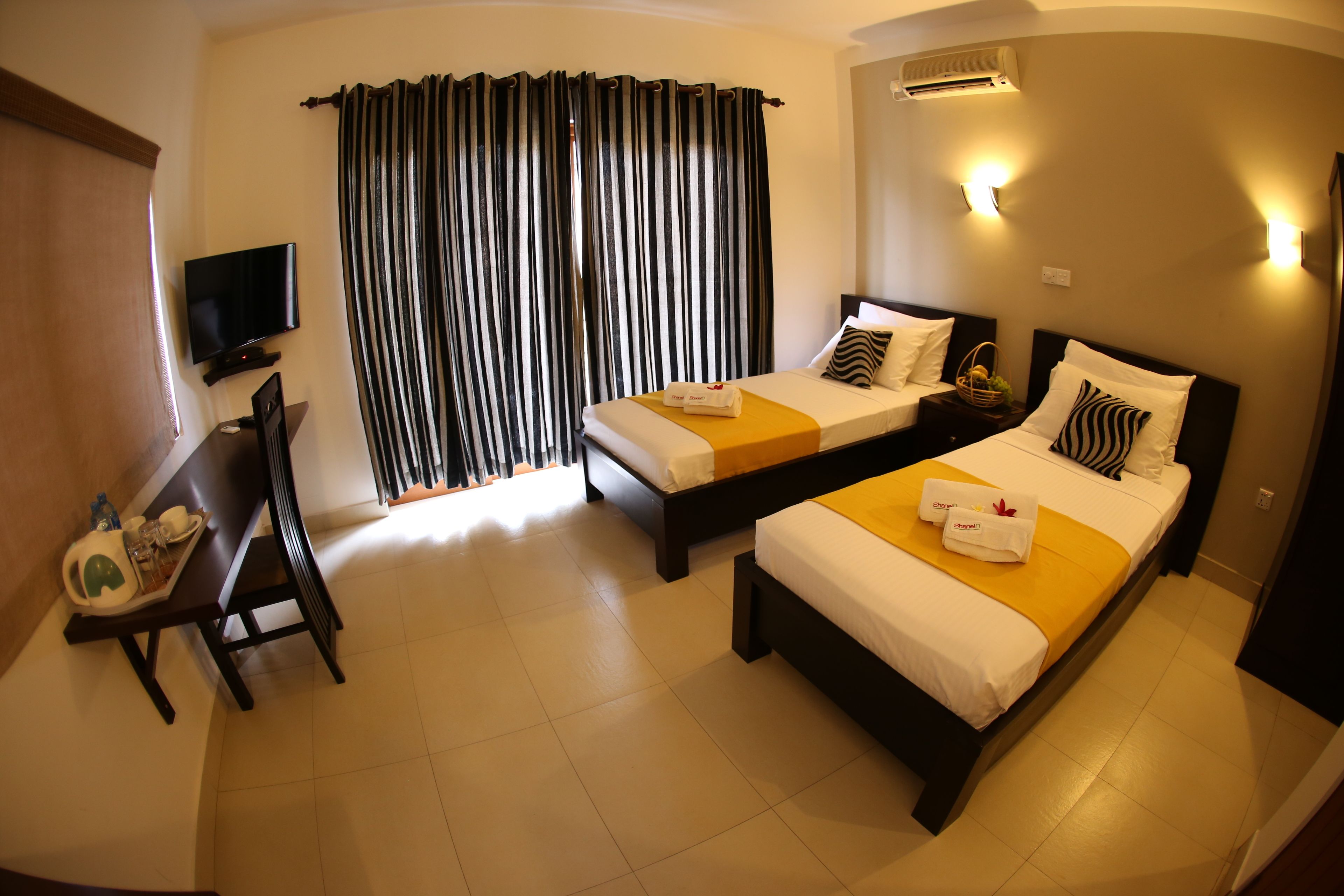 A hotel room with two beds, a TV, a desk with a chair, and a dining table.