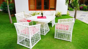 A white wicker outdoor seating area with a glass table, a bottle of champagne, and red cushions.
