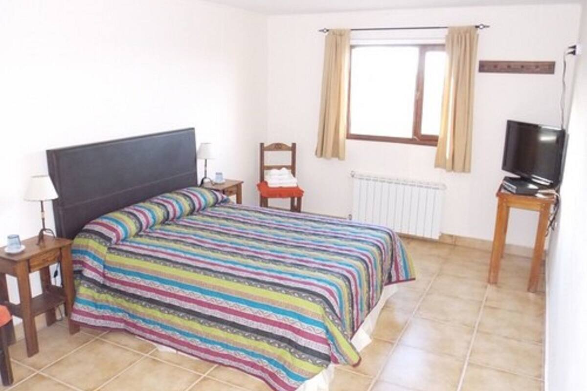 A bedroom with a bed, a TV, a chair, a lamp, and a window with curtains.