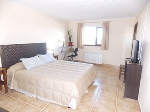 A bedroom with a bed, a desk, a chair, a radiator, and a television. - Hotel Mora (Los Antiguos)