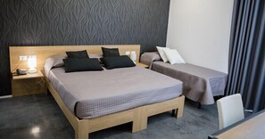 Habitación de hotel con una cama grande, una cama más pequeña, una mesita de noche con lámpara y un escritorio con silla.