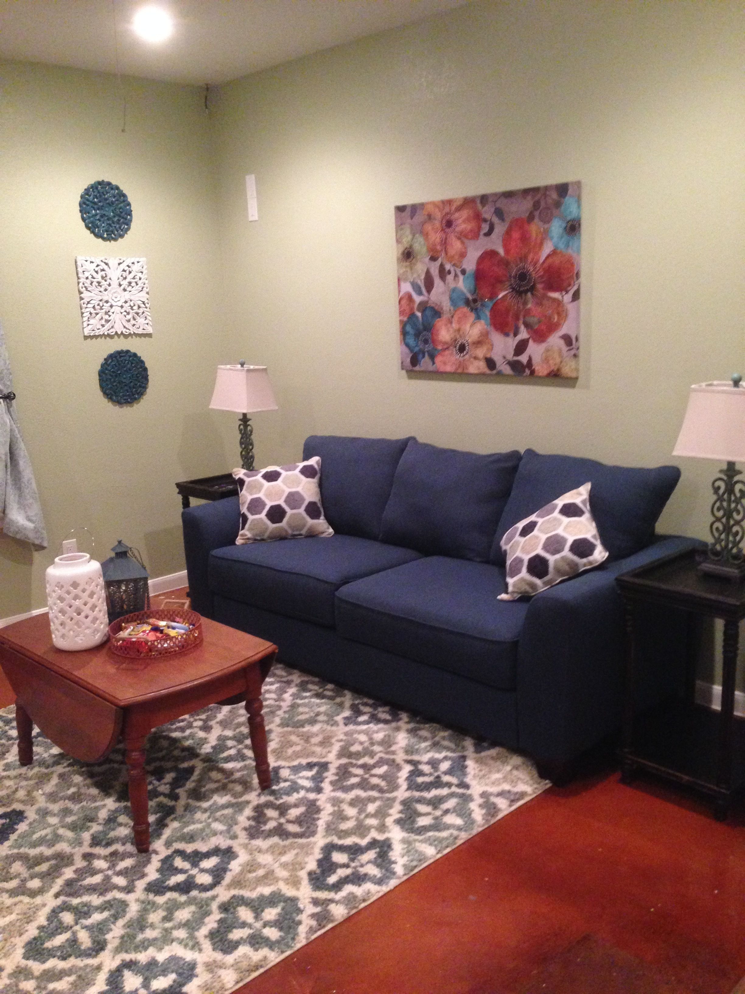 A living room with a blue sofa, patterned rug, decorative wall art, and two side tables with lamps.