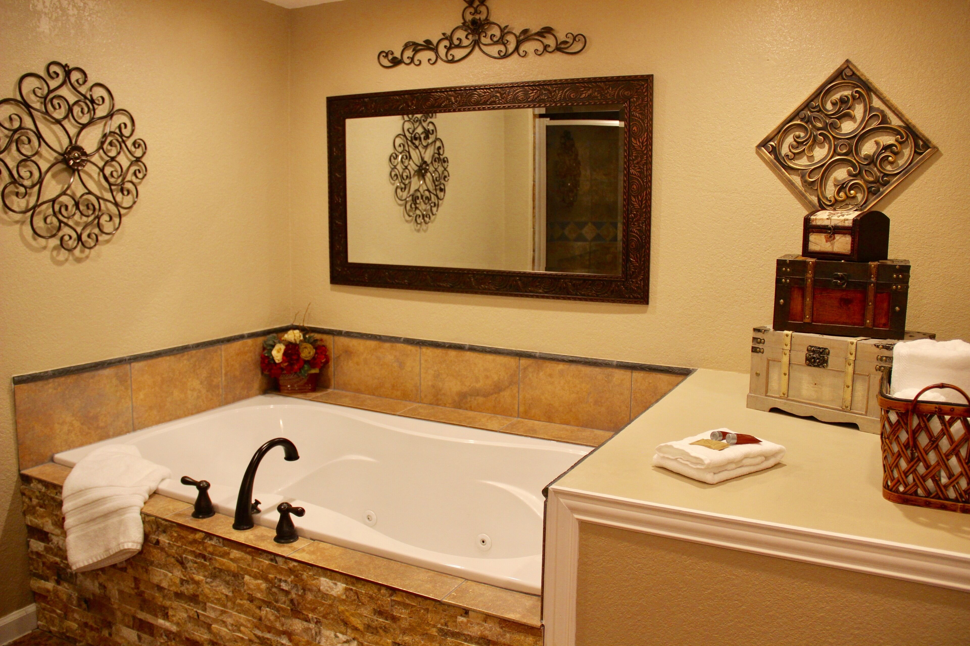 A bathroom with a large bathtub, a vanity with a mirror, and decorative wall art.