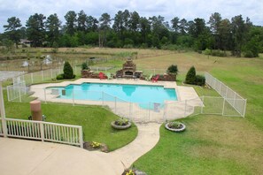 A backyard with a swimming pool, a stone fireplace, and a fenced area with chairs. - Maple Creek Bed and Breakfast (Tomball)