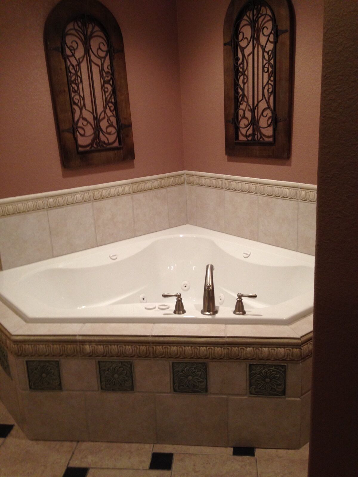 A large freestanding bathtub in a corner with a decorative wall and two arched windows.