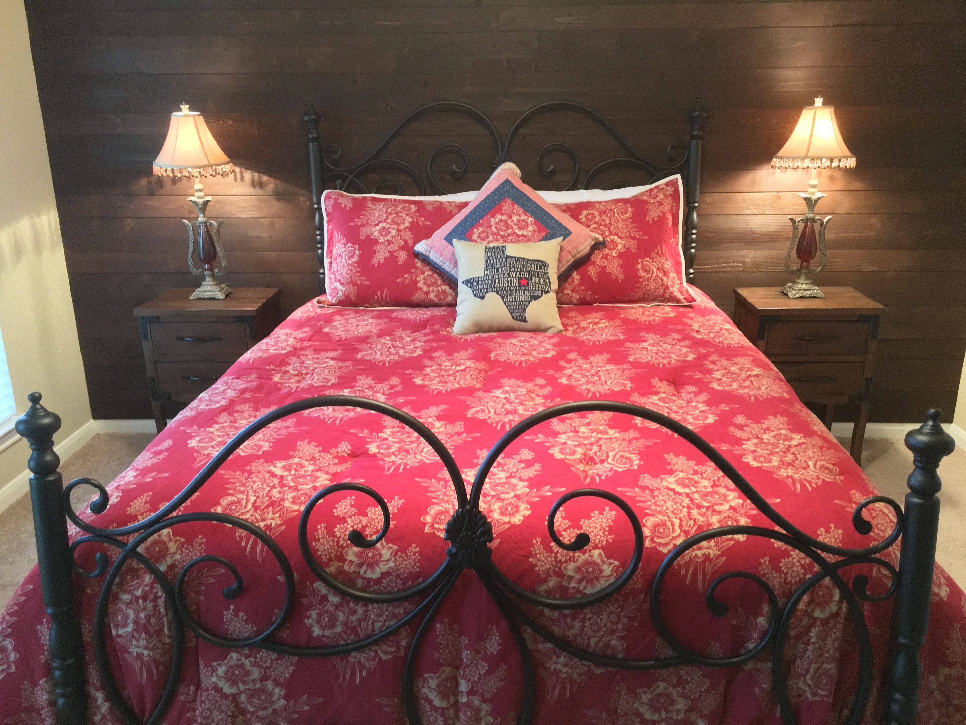 A bed with a red floral bedspread, black metal headboard, and two bedside tables with lamps.