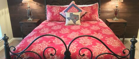 A bed with a red floral bedspread, black metal headboard, and two bedside tables with lamps.