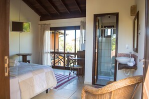 A hotel room with a bed, a desk, a chair, a bathroom with a sink, and a shower. - Pousada Gaia (Imbituba)