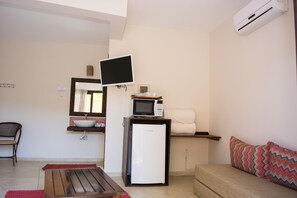 Un espacio habitable compacto con kitchenette, televisor de pantalla plana sobre la encimera, refrigerador, sofá y mesa de madera.