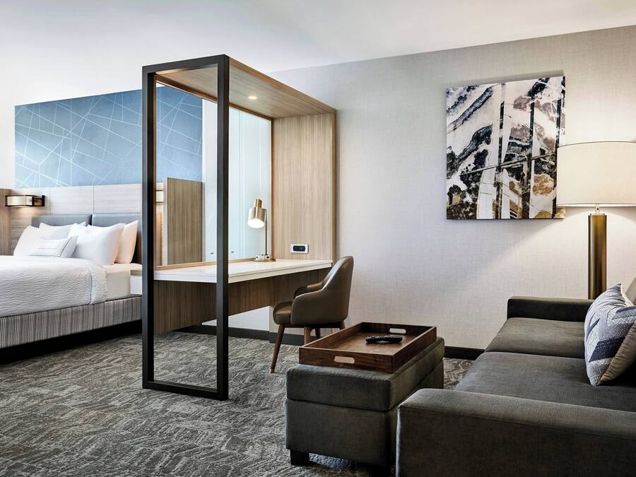 A hotel room with a bed, a desk, a sofa, and a large abstract painting on the wall.